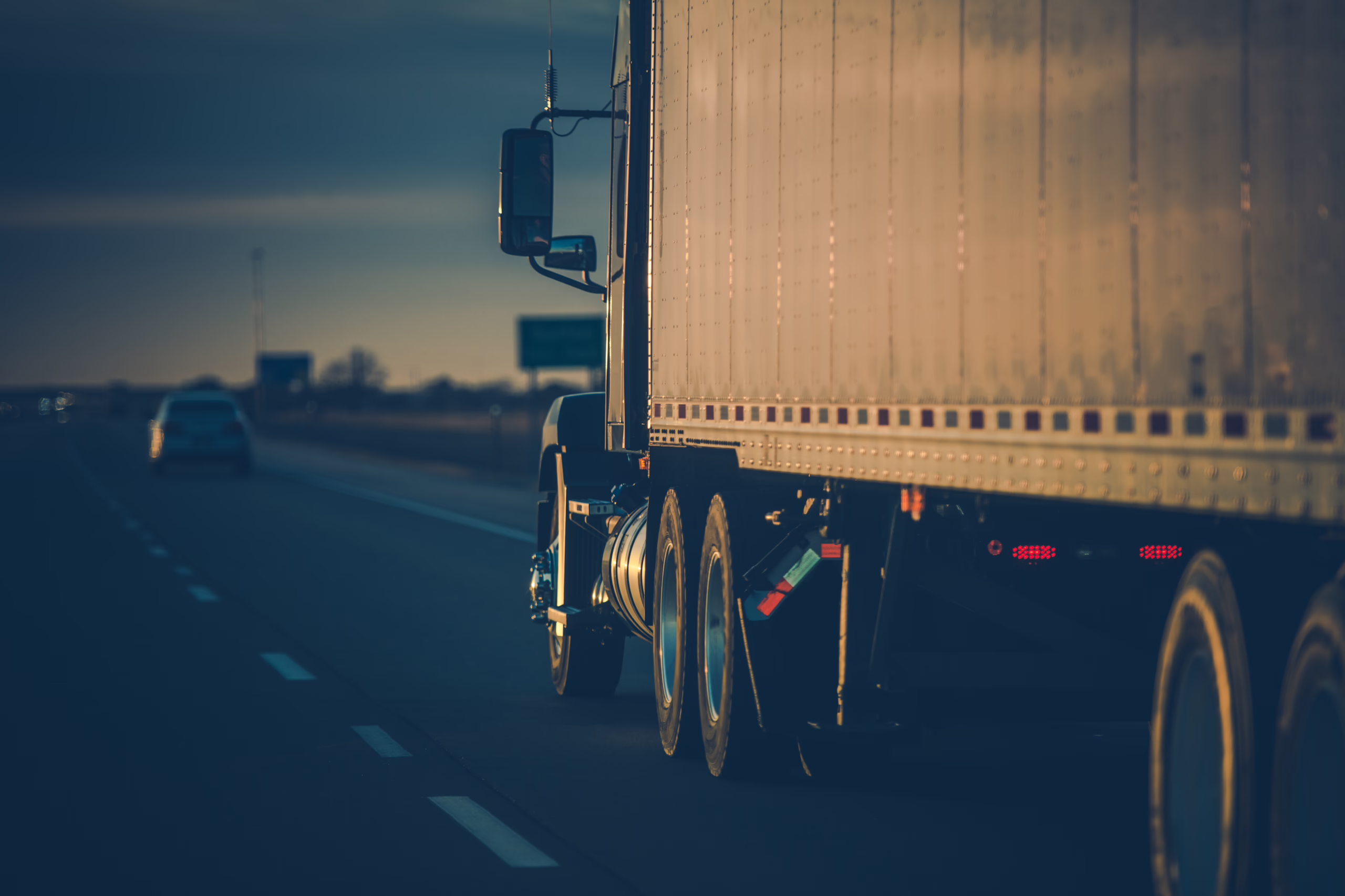semi truck and trailer driving down a highway at sunset