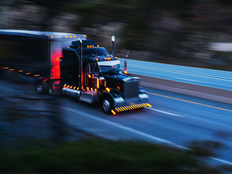 Semi truck and trailer with lights on driving down a highway