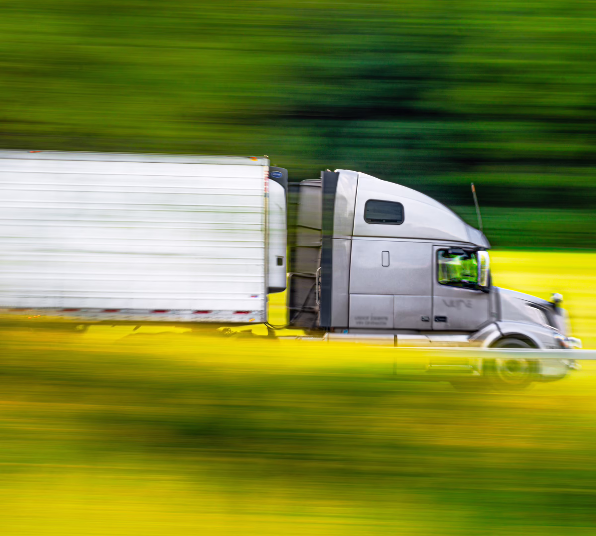 Semi truck and trailer driving down a road with greenery in the background
